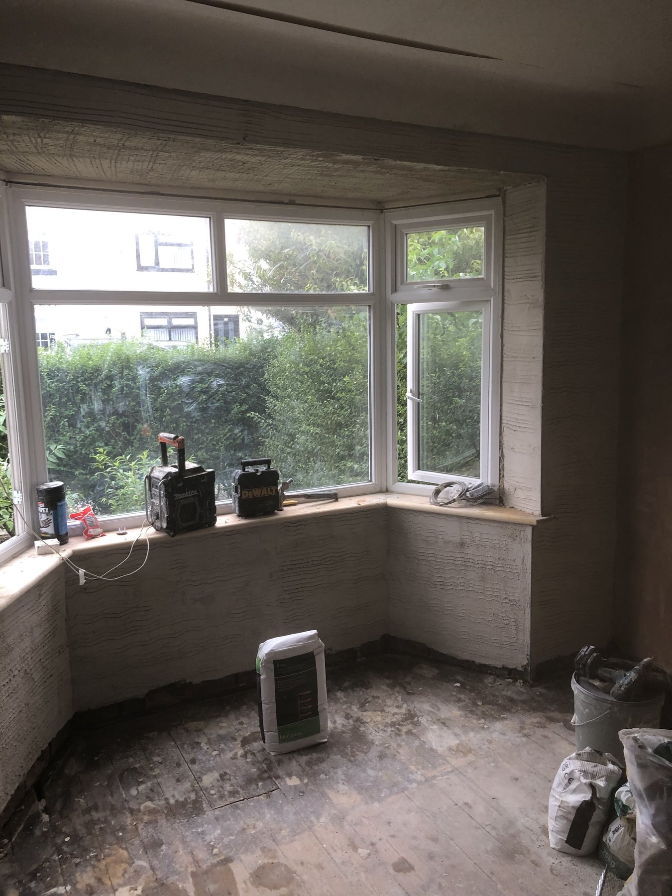A bay-windowed room with the walls in their first coat of plaster