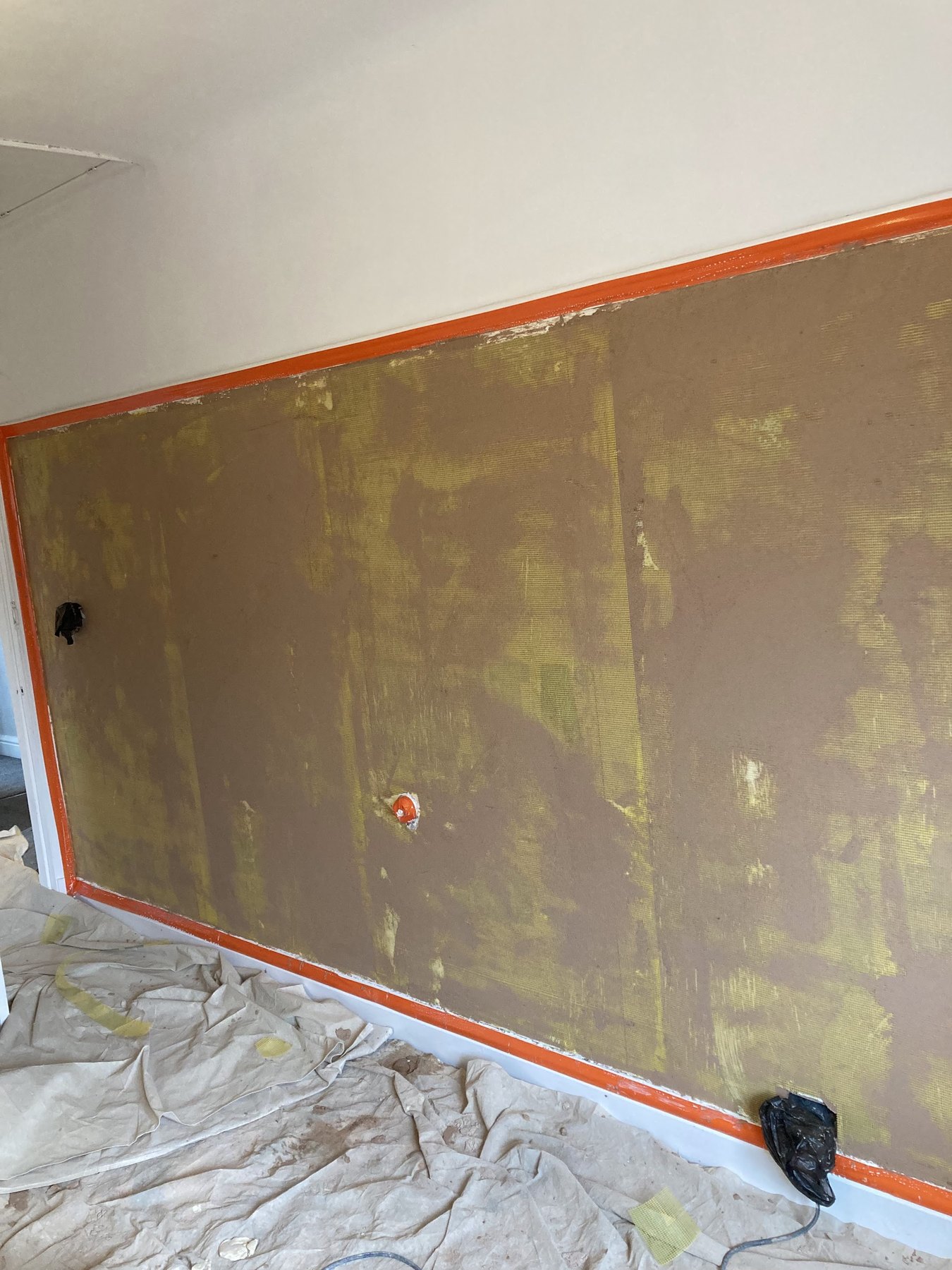 A wall sealed and taped off at the edges before plastering, dust sheets on the floor